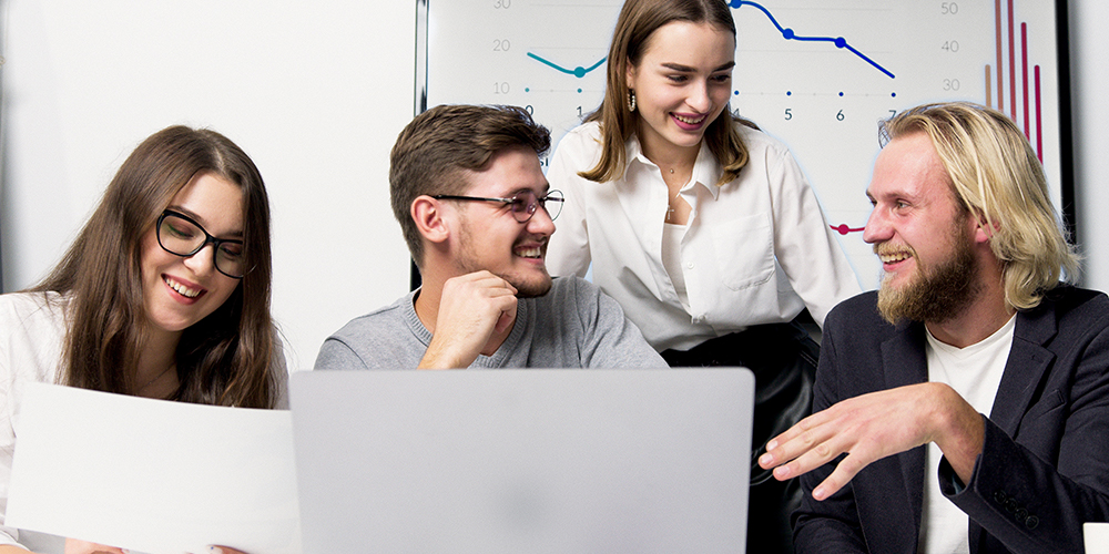Four people around a computer with chart behind them talking with data visualization to guide them.