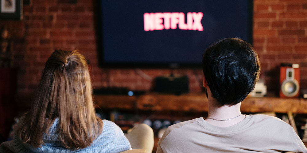 Two people watching Netflix on a TV while seated on a couch.