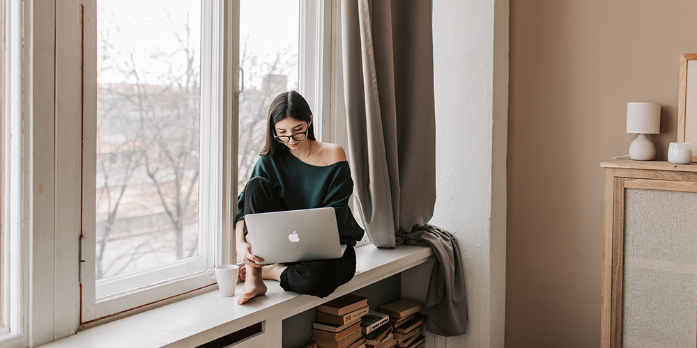 Woman on laptop in window seat, looking at proptech sites online.