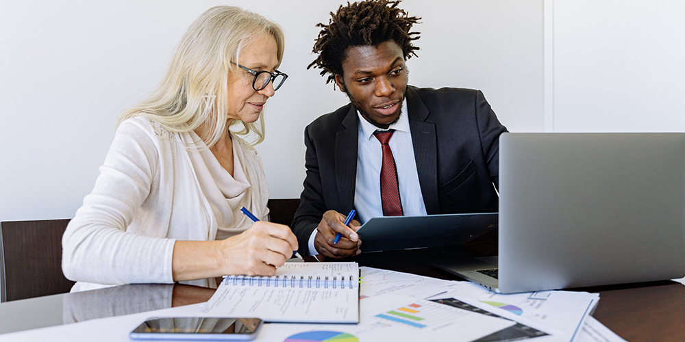 Realtors across demographics looking at data on laptop with papers scattered across desk.