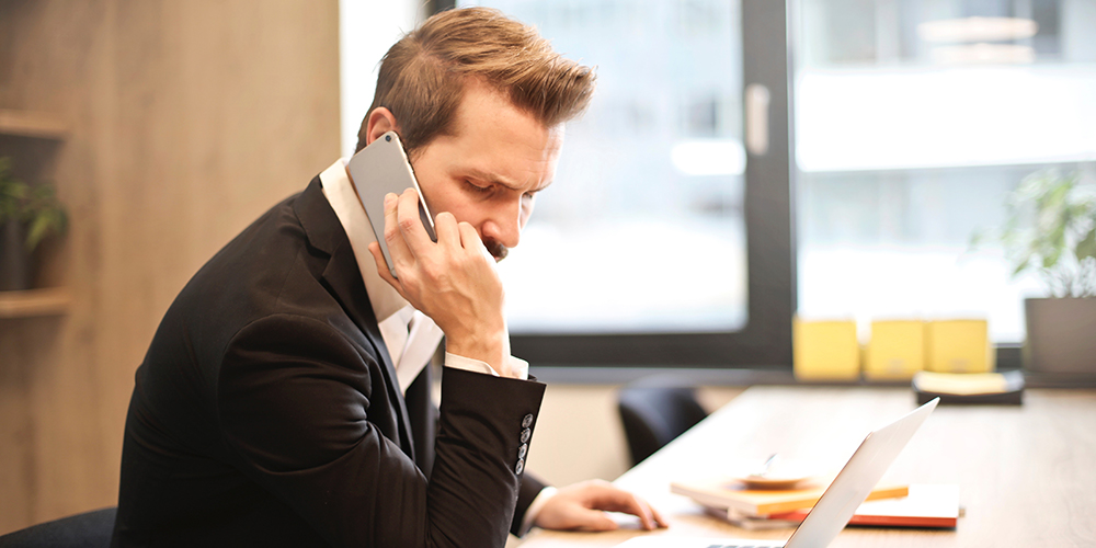 Man on the phone in front of a laptop, making sales call.