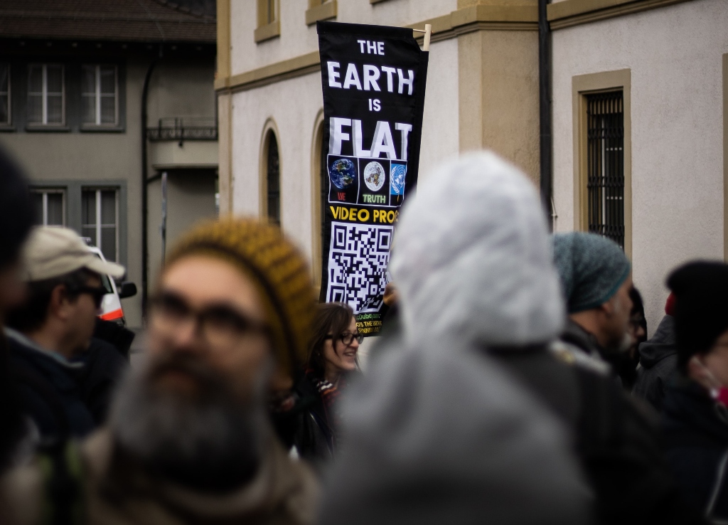 earth is flat sign in the middle of a crowd representing attach of personal beliefs