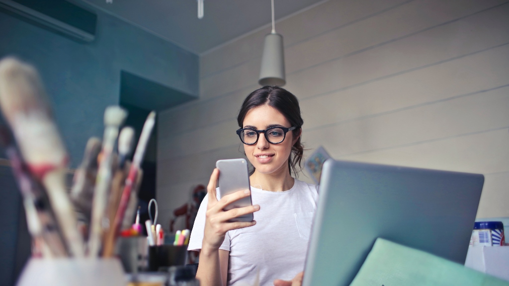 Person looking at phone with clutter on desk, not representing a clean work space.