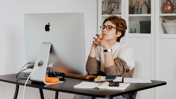 A woman sits in front of a desktop computer with a critical expression as she reads through an email to detect scams