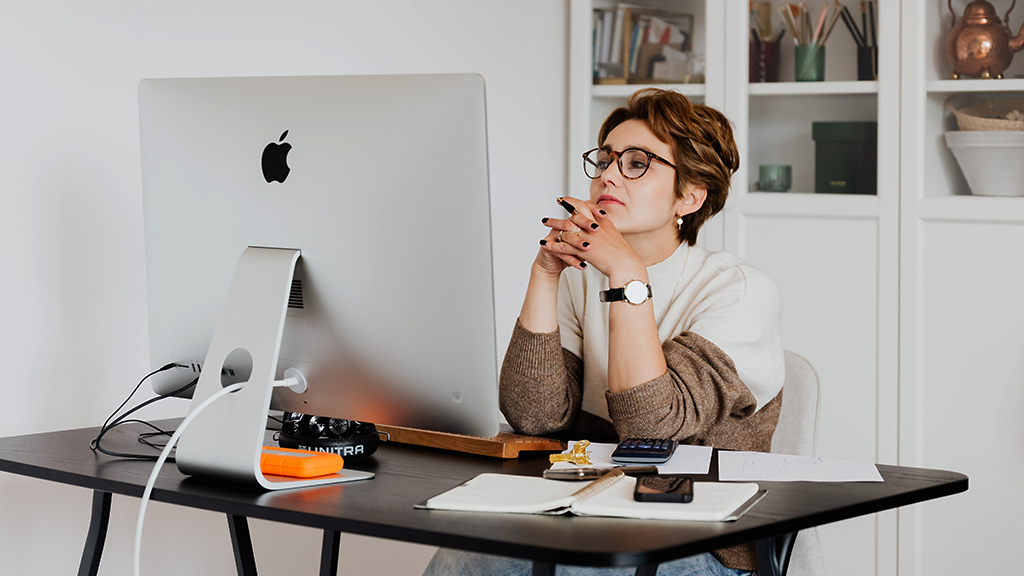 A woman sits in front of a desktop computer with a critical expression as she reads through an email to detect scams