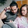 A man and a woman surrounded by moving boxes reviewing documents with contemplative expressions.