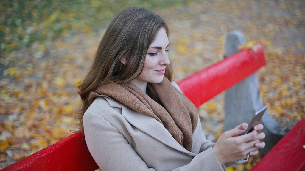 A woman sitting on a red park bench in the fall using her smartphone setting up moving.