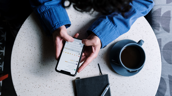 A person holds their smartphone above a table next to a coffee cup. The phone is open on a social media feed, reading comments.