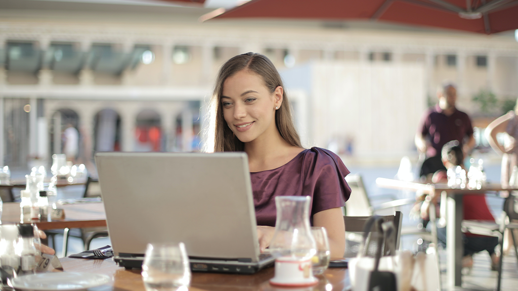 Woman typing at a computer in a brightly lit cafe, moderating Facebook comments with better tools.