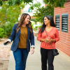 Two women walking down the street in an active conversation. One woman holds a phone in her hand while she considers giving her phone number.