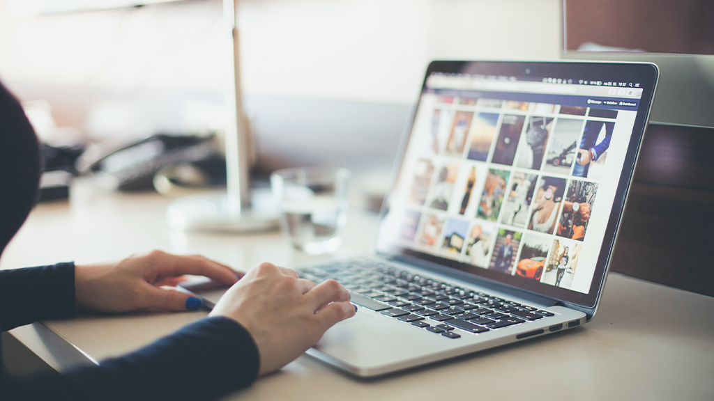 A laptop open with a person moving the mouse over a spread of digital content and images online.