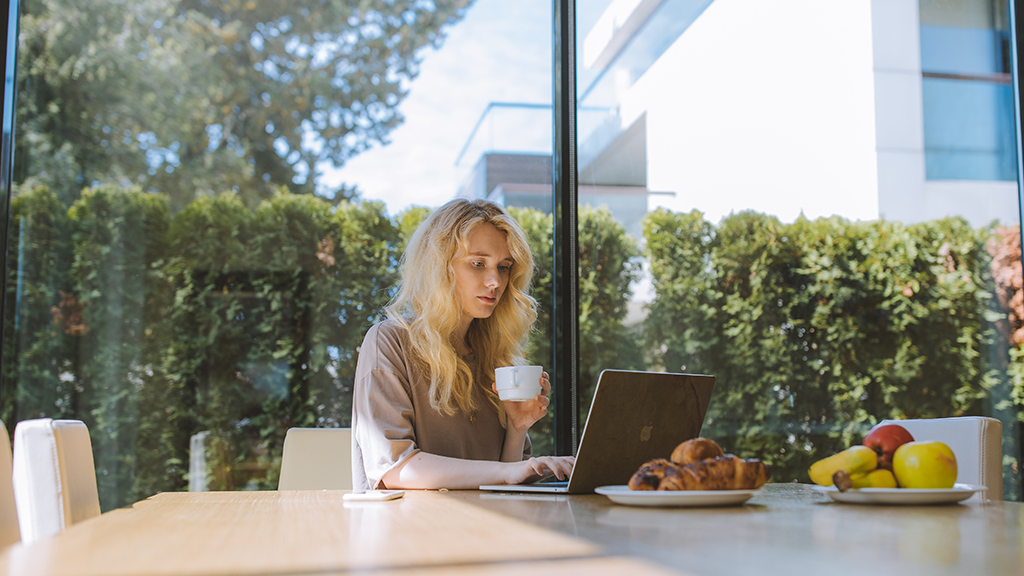 A woman sits at a laptop in a warmly lit kitchen with free time at a home work.