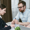 A man and a woman signing a document with the guidance of a woman helping with mortgages.