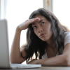 A woman sits at a computer with a hand to her forehead, with a thoughtful expression about AI