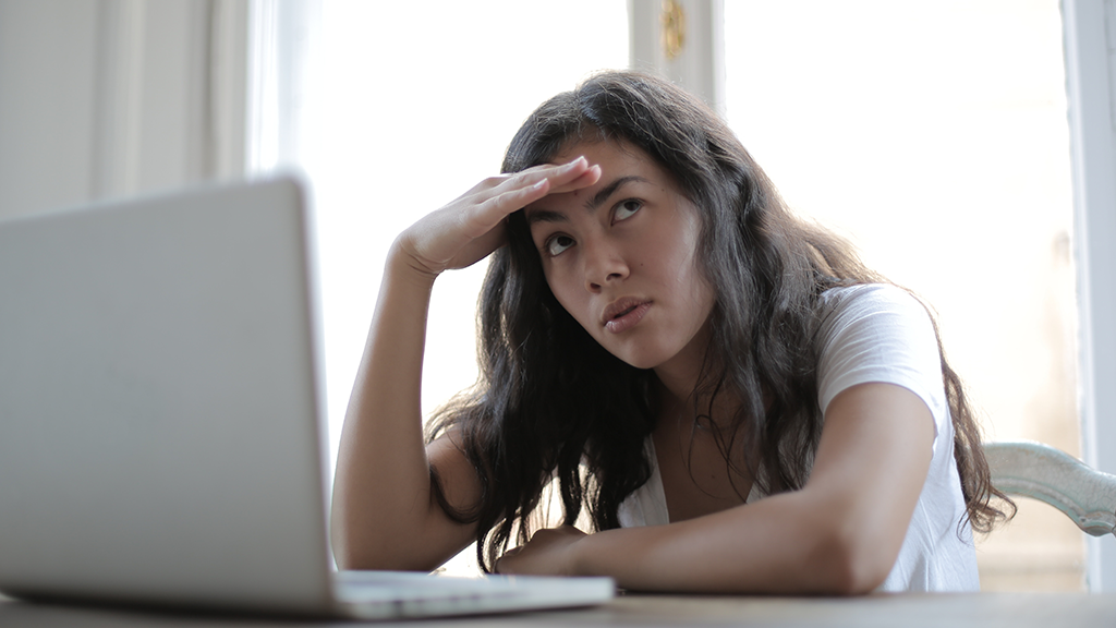 A woman sits at a computer with a hand to her forehead, with a thoughtful expression about AI