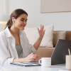 A woman waves at the laptop with airpods in as she checks in for daily stand-ups.