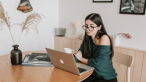 A woman sits at a desk with a laptop and a brushy plant sits next to her as she browses paid search conversions.