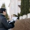 A woman stands in front of a house holding a clipboard as she reviews the documents of home sales.