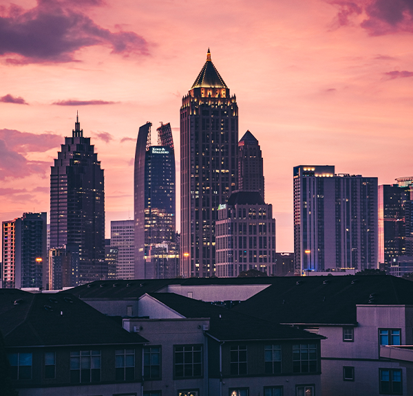 A sunset view of the Atlanta downtown skyline, with housing options in the distance among the pink and purple sky.
