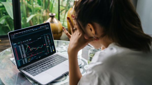 A woman reads a chart of interest rates, looking over her shoulder at the varying lines and tables, with her head resting in her hands in a stressed gesture