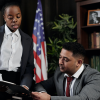 A man at a desk in a formal office reviews a book of law documents from a woman who is pointing out specific parts about the National Association of Realtors.