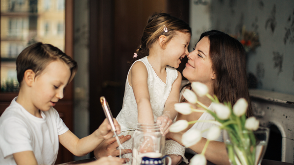 A mother holds her daughter while her son plays off to the side as they reside in their home.