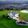 An overhead view of a large country home surrounded by green fields, with trees in the field beyond, on prime real estate.