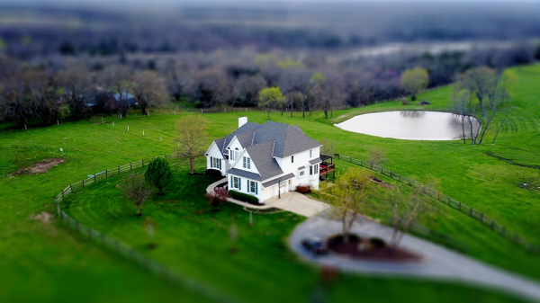 An overhead view of a large country home surrounded by green fields, with trees in the field beyond, on prime real estate.