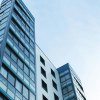 A skyward pointing view of two tall office buildings against a cloudy blue sky.