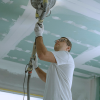 A construction worker sanding the interior ceiling of a house to avoid an OSHA violation.