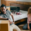 A man and a woman unpacking boxes inside of a house after dealing with landlords sexually harassing them.