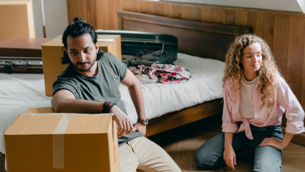 A man and a woman unpacking boxes inside of a house after dealing with landlords sexually harassing them.