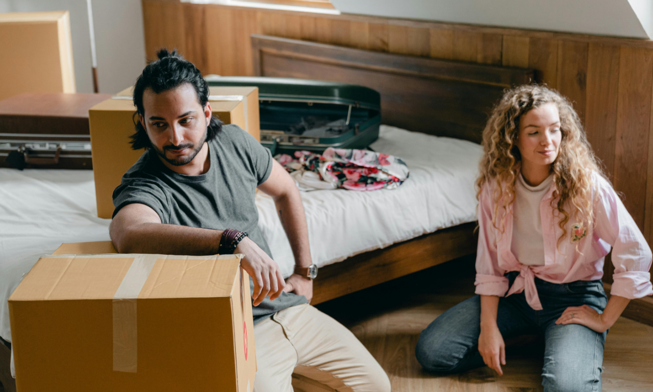 A man and a woman unpacking boxes inside of a house after dealing with landlords sexually harassing them.