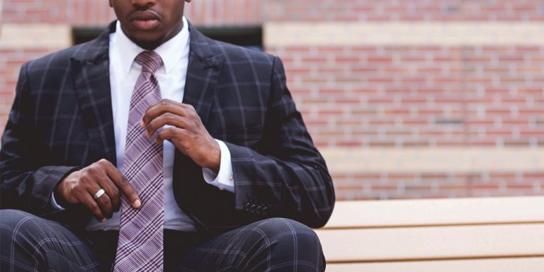 Black man in a suit seated with brick wall behind him.