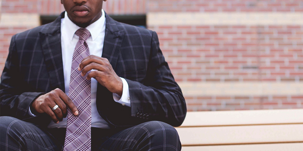 Black man in a suit seated with brick wall behind him.