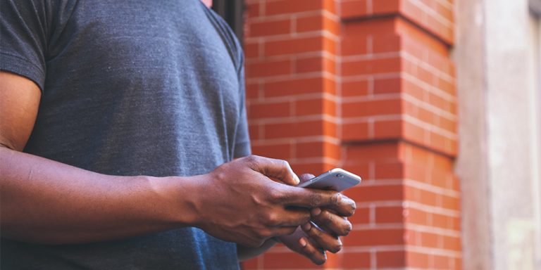 Man texting chatbots leaning against a brick wall.