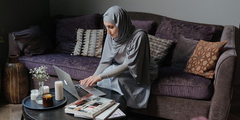 Woman in hijab sitting on couch, working from home on a laptop