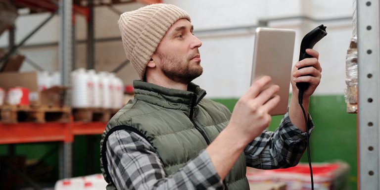 Man scanning inventory with tablet in one hand and a scanner in the other.