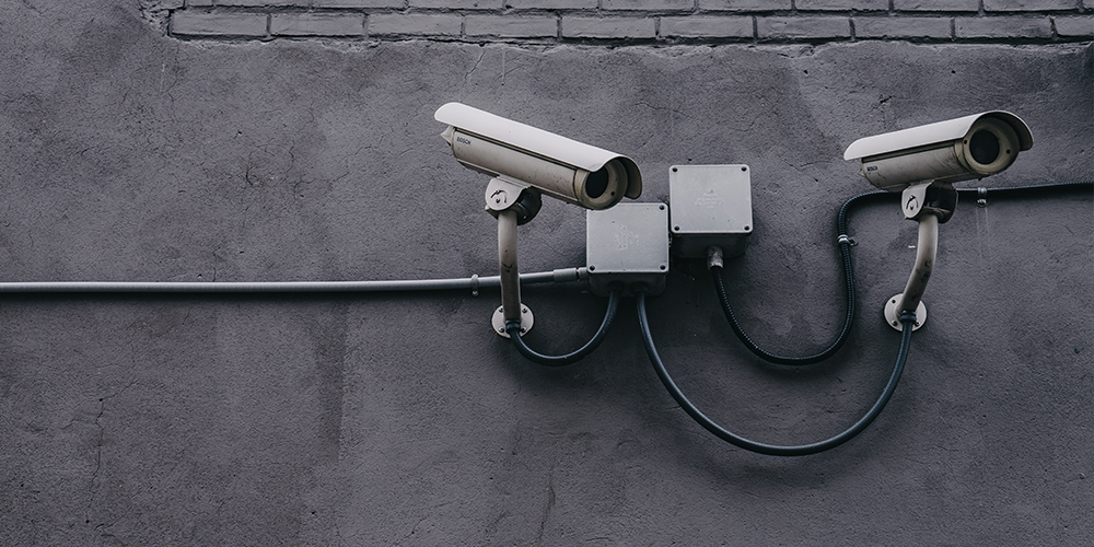 Security cameras on a gray cement wall that can be outfitted with AWS Panorama to give machine learning.