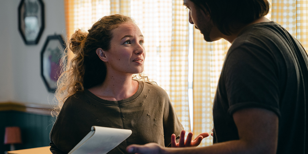 Stressed couple discussing options during unemployment in dimly lit room.