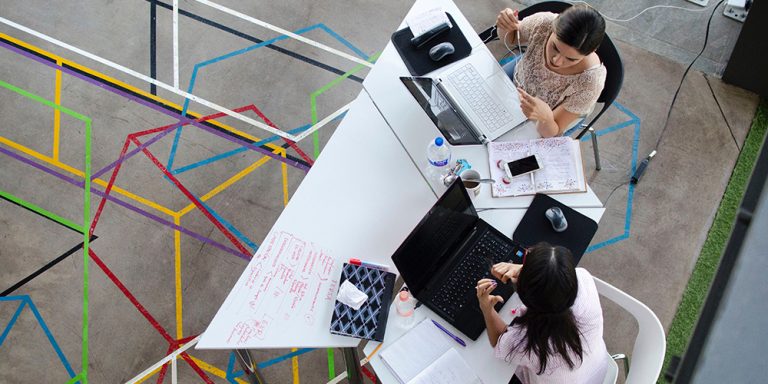 Birds eye view of two women networking at a table with colorful interconnecting pattern on a concrete floor.