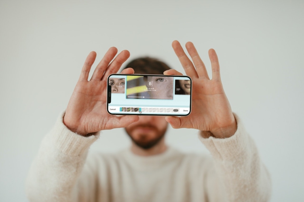 Caucasian man holding iPhone showing Canva video editor on mobile. 