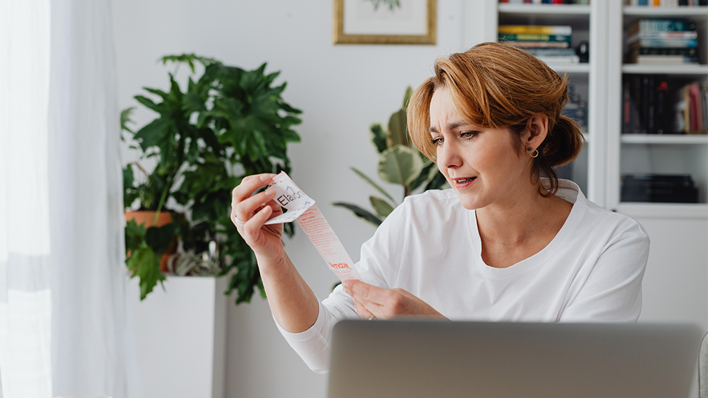 A woman sits in a modern white office reading a receipt with concerns about inflation.