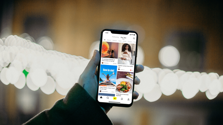 A hand holding a phone up against a nighttime scene with stringlights. The phone is open to the Lemon8 app from Bytedance.