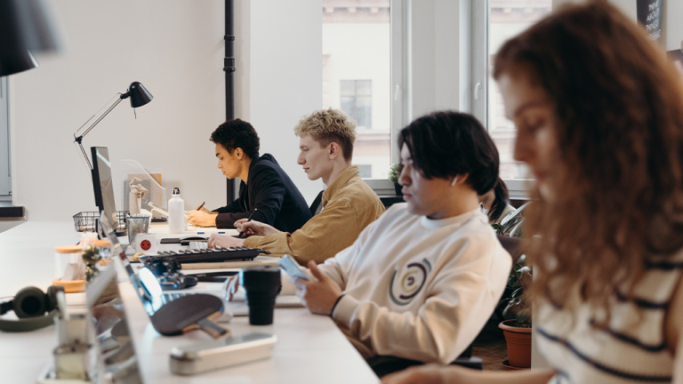An open office layout with several people all on the same table typing at a computer, with generative AI assisting their workflow.