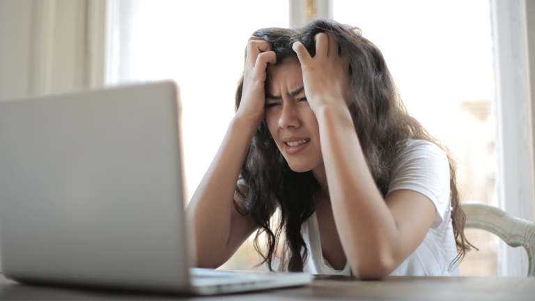 A person looking at a job application and running their hands through their hair in frustration