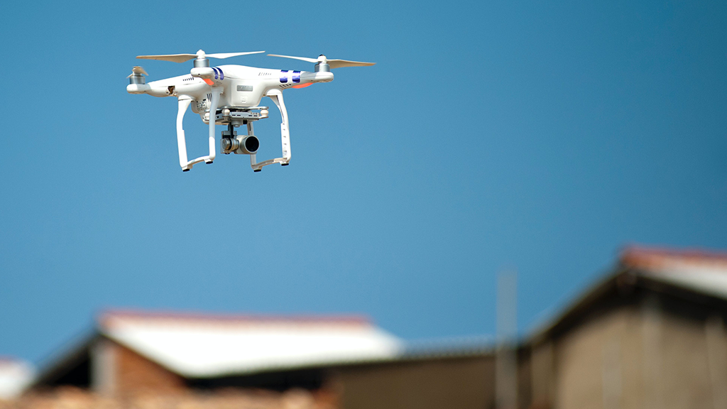 A drone flying over a set of houses. The camera is focused on the drones, while the neighborhood is blurred.