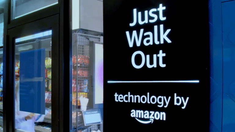 A close up view of a grab and go shopping area with a sign reading Just Walk Out, technology by Amazon on a black sign.